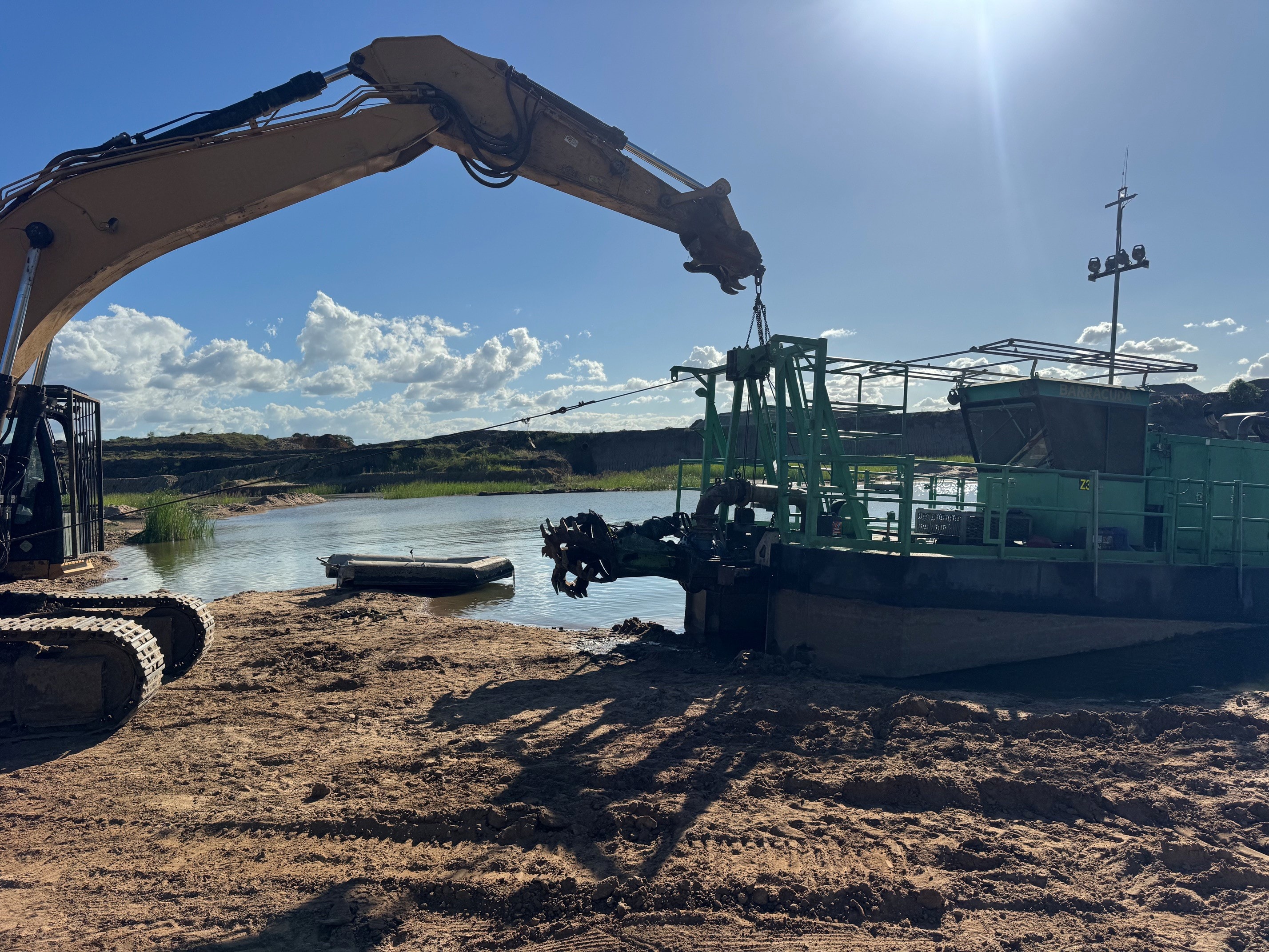 Excavator working alongside dredge barge on waterway
